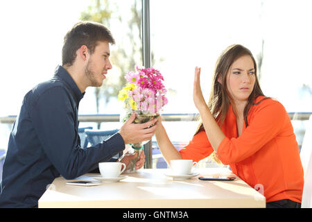 Man bat um Vergebung bietet einen Blumenstrauß für seine Freundin in einem Café mit einem äußeren Hintergrund Stockfoto