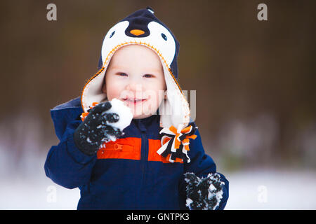 Ein kleiner Junge hält einen Schneeball und tragen ein Winter-Mantel und Hut lächelt, als er die Kamera schaut. Stockfoto