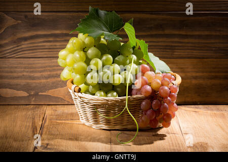 Grün und rosa Trauben im Korb auf hölzernen Hintergrund. Stockfoto