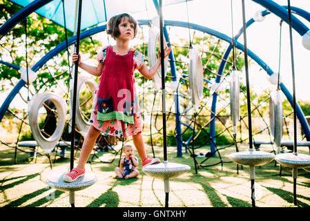 Mädchen spielen auf Spielplatz im schönen Abendlicht mit Baby im Hintergrund Stockfoto