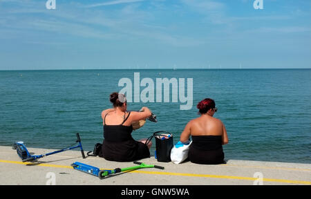 zwei Frauen sitzen auf Barriere Wand in Küsten Stadt Herne Bay im Osten Kent uk august 2016 Stockfoto