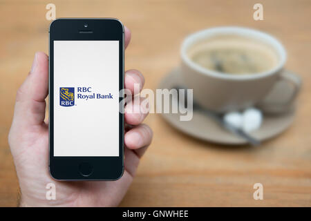 Ein Mann schaut auf seinem iPhone die RBC Royal Bank-Logo anzeigt, während bei einer Tasse Kaffee (nur zur redaktionellen Verwendung) saß. Stockfoto