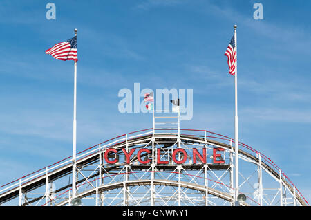 Höchste Gipfel der die denkmalgeschützte alte Cyclone Holzachterbahn in Coney Island mit amerikanischen Fahnen und Zeichen Stockfoto