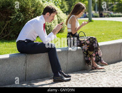 Ein Mann und Frauen auf Mittagspause überprüfen Sie ihre Telefone. London, UK. Stockfoto