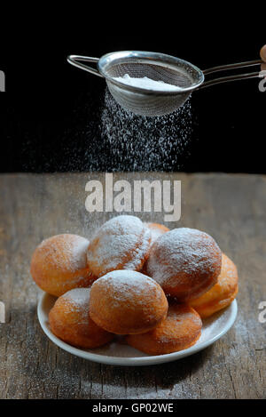 gießt Zucker mit Sieb über donuts Stockfoto