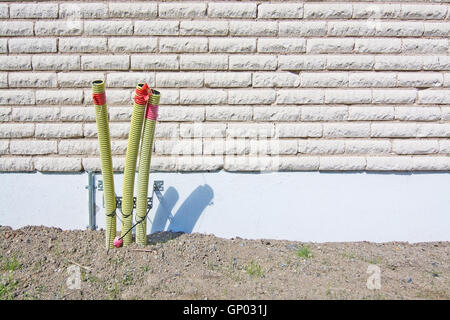 Elektro Schutzrohre ragte aus dem Boden in der Nähe von einem weißen Backstein-Haus. Stockfoto