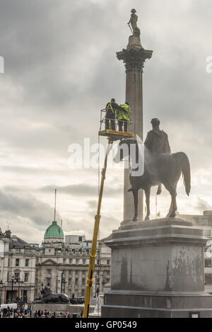 Handwerker Reinigung der Statue von König George IV Statue an einem bewölkten Nachmittag. Lord Horatio Nelson kann auf eine Spalte im Hintergrund gesehen werden. Stockfoto