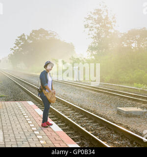 An einem nebligen Tag Sonnenschein eine asiatische Frauen Reisende warten auf einen Zug auf der Plattform am örtlichen Bahnhof. Stockfoto