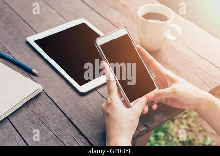 Die Hand der Frau hält Telefon und Telefon auf Tisch im Garten im Coffee Shop mit Jahrgang abgeschwächt. Stockfoto