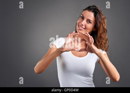 Eine schöne junge Frau lächelt während Gestaltung Herzen mit ihren Händen Stockfoto