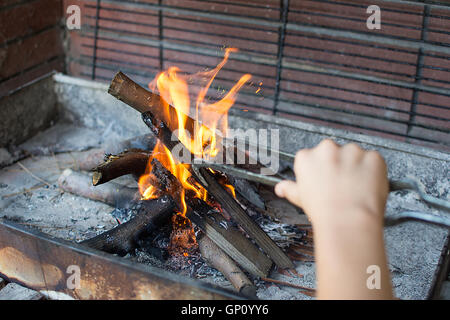 Starten Sie Feuer für Holzkohle-Grill. Arm mit langstieligen Zangen Einstellung Feuer Closeup. Helle Flammen und Brennholz. Bekommen Sie Ihre Gri Stockfoto