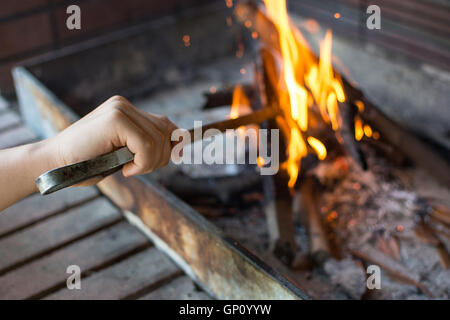 Starten Sie Feuer für Holzkohle-Grill. Arm mit langstieligen Zangen Einstellung Feuer Closeup. Helle Flammen und Brennholz. Stockfoto
