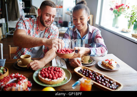 Glückliches Mädchen bietet Kerl zu einigen frischen Himbeeren aus der Schüssel nehmen Stockfoto
