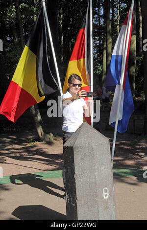 Frau nimmt ein Foto von sich selbst mit den Flaggen der Niederlande, Belgien und Deutschland vor dem Boarder-Stein an der Stelle "Intakter" in der Nähe von Aachen, im Dreiländereck Deutschland, Niederlande und Belgien. Dieser Spot ist der höchste Punkt der Niederlande (322 m). Stockfoto