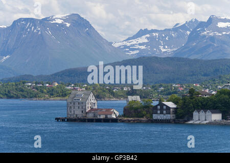 Blick über den Hafen von Alesund in Norwegen; einige Gebäude im Vordergrund, Schnee bedeckte Berge nach hinten. Stockfoto