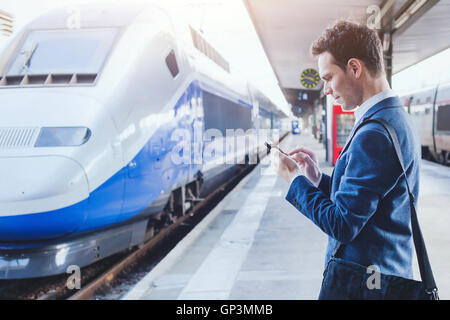 Mann mit mobilen Anwendung auf seinem Smartphone am Bahnhof, Geschäftsreisen Stockfoto