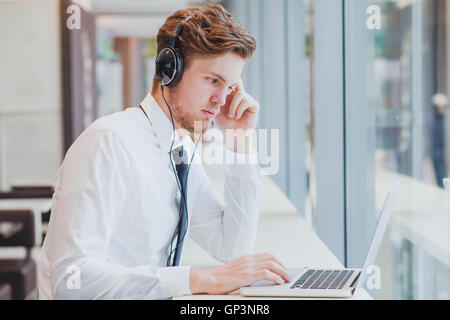 Geschäftsmann in Kopfhörer arbeiten mit Laptop im modernen Café-Interieur Stockfoto