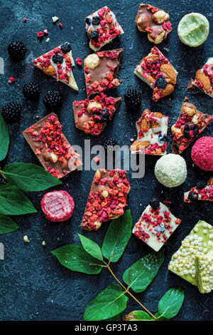 Schokolade bellt mit getrockneten Früchten (Erdbeeren, Raspberris, Gojibeeren, Blaubeeren), Nüssen und Getreide. Ansicht von oben, über Kopf. Stockfoto