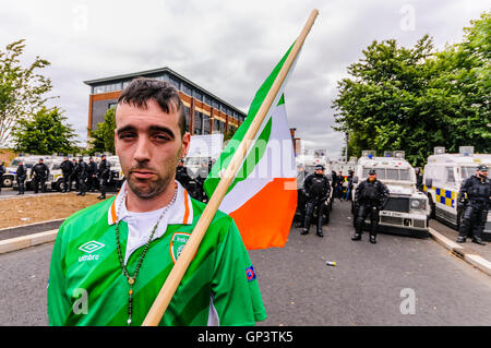 Ein Irish Republican Mann hält eine dreifarbige Fahne und tragen ein Irland Fußballtrikot und Satz von Rosenkranz, ist daran gehindert, zu Fuß ins Stadtzentrum von Belfast durch eine Linie von PSNI Polizisten Stockfoto