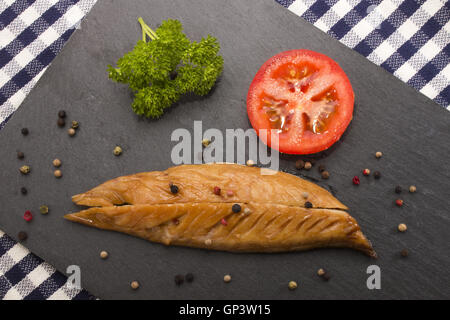 geräucherte Makrele mit eine Scheibe Tomate, Petersilie und gemischten Pfeffer auf dem Schiefer Teller Stockfoto