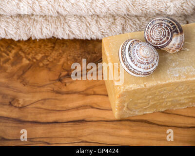 Selbstgemachte Seife, zwei Schneckenhäuser und Terry Handtuch auf den Olivenbaum texturiert Holzbrett Stockfoto