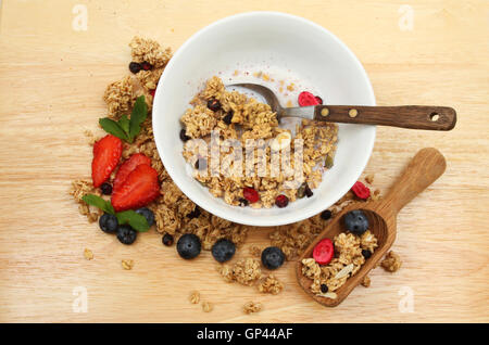 Müsli mit Milch in einer Schüssel auf einem Brett mit frischem Obst und eine hölzerne Kugel Stockfoto