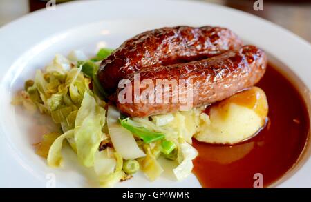 Würstchen und Kartoffelbrei mit saisonalen Gruenen mit Rotwein Soße auf einem weißen Teller serviert - Filter angewendet Stockfoto