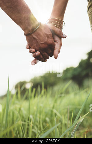 Vertikale Aufnahme des jungen Paares zu Fuß durch Wiese hand in hand mit Sonne flare. Nahaufnahme Schuss mit Fokus auf die Hände des Mannes und w Stockfoto