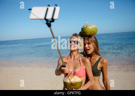 Zwei junge Frauen, die Aufnahme mit Smartphone auf Selfie Stick am Strand. Freundinnen im Bikini Sommer Ferien auf th Stockfoto