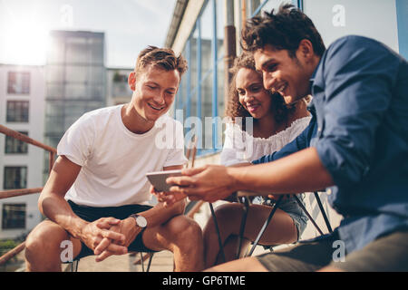 Gruppe von Menschen, die Videos auf dem Handy beim Sitzen am Café im Freien. Drei junge Freunde sitzen im Freien und looki Stockfoto