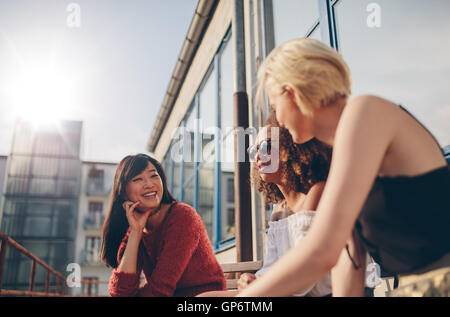 Gruppe von Freundinnen reden auf einer Terrasse. Drei junge Frauen treffen im Café im Freien, plaudern und genießen. Stockfoto