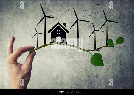 Menschliche Hand halten einen Ast. Ökologische grüne Energiekonzept. Silhouette von Haus, Windturbine und Vögel fliegen Stockfoto