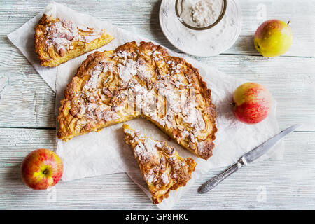 In Scheiben geschnitten hausgemachte Apfel und Mandelkuchen auf hölzernen Hintergrund. Frisches Obst und Puderzucker, Ansicht von oben Stockfoto