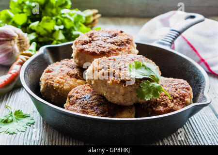 Huhn gebraten Koteletts in schwarzem Gusseisen Pfanne, frisches Gemüse und Petersilie auf hölzernen Hintergrund Stockfoto