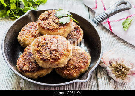 Hausgemachte Schnitzel, gebraten oder gebacken in schwarzem Gusseisen Pfanne. Holztisch, frisches Gemüse und Petersilie Stockfoto