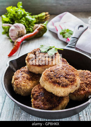 Hausgemachte Huhn gebraten Koteletts in schwarzen gusseisernen Pfanne auf hölzernen Hintergrund und rohem Gemüse. Stockfoto