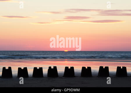 Linie von Sandburgen Silhouette bei Sonnenaufgang am Strand. Northumberland, England Stockfoto