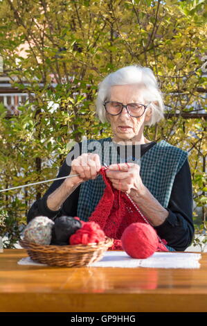 Ältere Frau stricken mit roter Wolle im freien Stockfoto