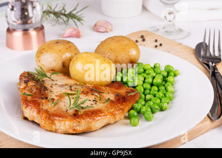 Schweinekotelett, gekochte Pellkartoffeln und grüne Erbsen auf dem Silbertablett serviert Stockfoto