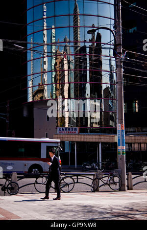 Ein Fußgänger geht vorbei an Gebäuden reflektiert in einem Bürohaus Fassade in Tokio, Japan. Stockfoto