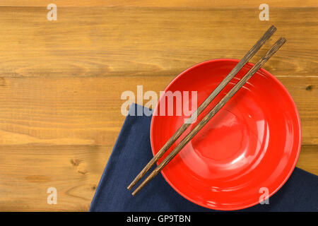 rote leere Schüssel mit Essstäbchen Holztisch und dunkle Blau napery Stockfoto