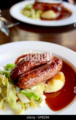 Würstchen und Kartoffelbrei mit saisonalen Gruenen mit Rotwein Soße auf einem weißen Teller serviert - Filter angewendet Stockfoto