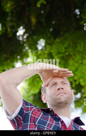 Verlässt der Mann Blick auf seine Zukunft mit seiner Hand über die Augen im Freien mit Grün im Hintergrund. Stockfoto