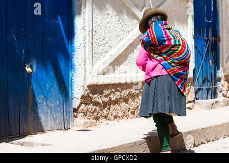 Maras Peru-Mai 18: einheimische Quechua-Frau mit schönen Farben, die zu Fuß in Richtung einer blauen Tür. 18. Mai 2016, Maras Peru. Stockfoto