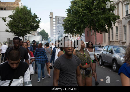 Gruppe von Freunden zu Fuß entlang Golborne Road mit Trellick Tower in der Ferne auf Sonntag, 28. August 2016 bei den 50. Notting Hill Carnival in Westlondon. Ein Fest der Westindischen / Karibik Kultur und Europas größte Straßenparty, Festival und Parade. Nachtschwärmer kommen in hunderttausenden zum Spaß haben, tanzen, trinken und loslassen in die tolle Atmosphäre. Es wird geführt von den Mitgliedern der West-indischen / Karibische Gemeinschaft, besonders die Trinidad und Tobagonian britische Bevölkerung, von denen viele seit den 1950er Jahren in der Gegend gelebt haben. Der Karneval hat bis zu 2 Millionen Menschen angezogen. Stockfoto