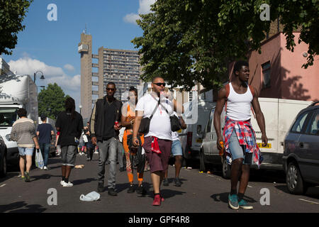 Gruppe von Freunden zu Fuß entlang Golborne Road mit Trellick Tower in der Ferne auf Sonntag, 28. August 2016 bei den 50. Notting Hill Carnival in Westlondon. Ein Fest der Westindischen / Karibik Kultur und Europas größte Straßenparty, Festival und Parade. Nachtschwärmer kommen in hunderttausenden zum Spaß haben, tanzen, trinken und loslassen in die tolle Atmosphäre. Es wird geführt von den Mitgliedern der West-indischen / Karibische Gemeinschaft, besonders die Trinidad und Tobagonian britische Bevölkerung, von denen viele seit den 1950er Jahren in der Gegend gelebt haben. Der Karneval hat bis zu 2 Millionen Menschen angezogen. Stockfoto