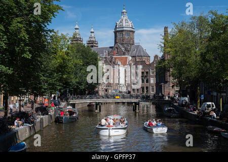 Kreuzfahrt auf einem Amsterdamer Kanal in das Rotlichtviertel gegen die Basilika des Heiligen Nikolaus Stockfoto