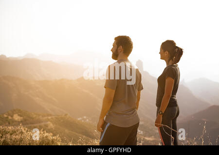 Zwei Jugendliche stehen und bewundern Sie die Aussicht auf einen Berg in der prallen Sonne mit ihren Händen an ihren Seiten Stockfoto