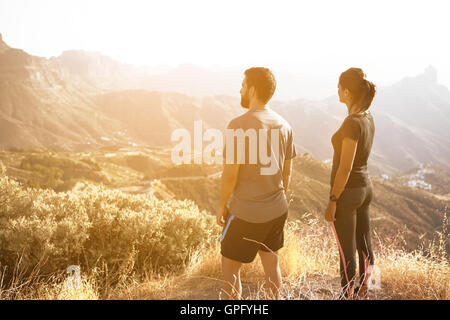 Zwei junge Menschen stehen und bewundern Sie die Aussicht auf einen Berg in der prallen Sonne mit ihren Händen an ihren Seiten Stockfoto