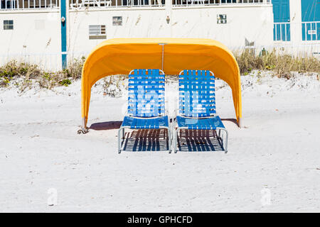 Blaue Liegestühle am Strand unter gelbe Sonnenschirme Stockfoto